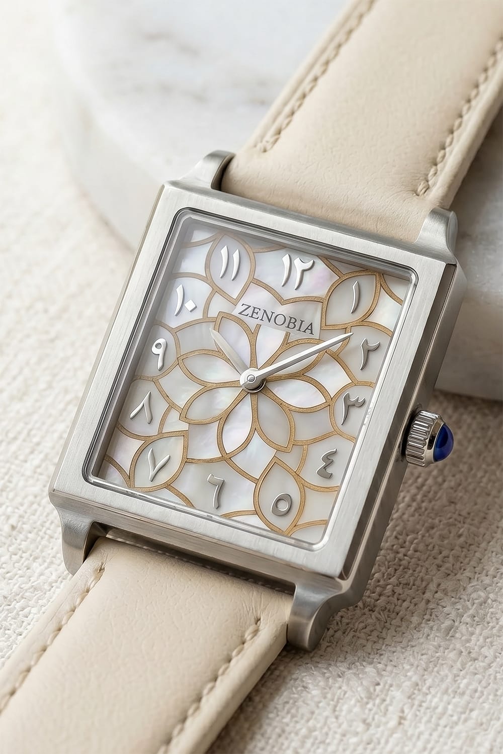 An angled view of a Zenobia watch with a luminous floral dial, rectangular silver-coloured case and ivory strap